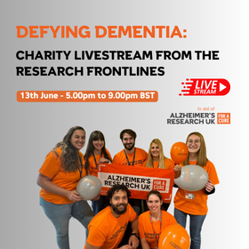 Promotional graphic for a charity livestream event titled "DEFYING DEMENTIA: Charity Livestream from the Research Frontlines." The event is scheduled for 13th June, from 5:00 pm to 9:00 pm BST, in support of Alzheimer's Research UK. The graphic features seven individuals, all wearing bright orange T-shirts, some holding balloons and a banner promoting Alzheimer's research. The layout includes large text and a livestream play button graphic, suggesting that the event will be broadcast online. The background is simple, emphasizing the text and the group of smiling volunteers.