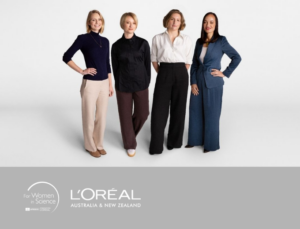 Four professionally dressed women stand side by side against a plain light background, smiling and facing forward. A banner below shows the For Women in Science logo and L’Oréal Australia and New Zealand branding.