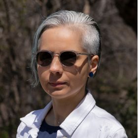Dr Arezoo Talebzadeh - DEMENTIA RESEARCHER Woman with short gray hair wearing sunglasses and a white jacket outdoors.