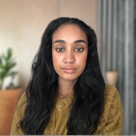 Nisha Ramjuttun - DEMENTIA RESEARCHER Portrait of a young woman with long dark wavy hair wearing a mustard yellow blouse, looking at the camera.