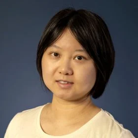Portrait of a woman with short dark hair, wearing a light beige top, against a blue background.