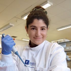 Adriana Perez Grovas Dr Adriana Perez Grovas wearing a white laboratory coat and blue gloves, holding a pipette in a laboratory.